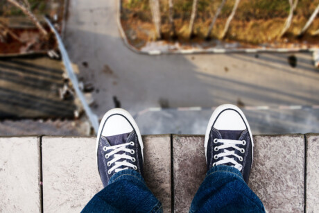 Person in Turnschuhen und Jeans stehen an einem Abgrund