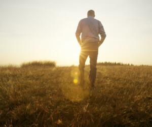 Mann läuft allein in der Abendsonne an einem Feld entlang