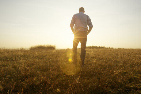 Mann läuft allein in der Abendsonne an einem Feld entlang